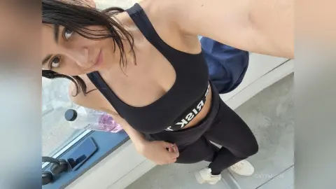 Young woman in black athletic wear posing for a selfie in a bright, modern indoor setting.