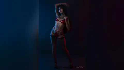 Tattooed woman in red bikini posing in moody blue studio lighting.