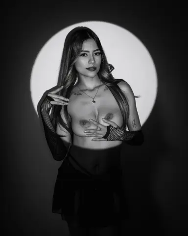 Young woman in black mesh gloves and dark skirt posing in dramatic monochrome lighting.