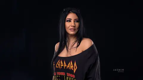MissyJolie poses with long black hair wearing a black rock-style t-shirt against a dark background.