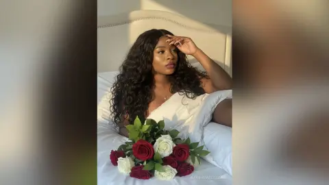 Beautiful woman with long wavy hair relaxing in bed with a bouquet of red and white roses in soft sunlight.