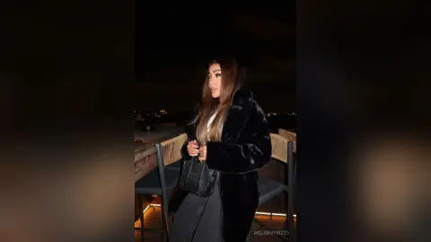 Stylish woman in a black faux fur coat and dark jeans posing on a rooftop at night.