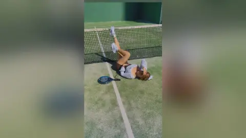 Young woman in white athletic wear relaxing on a green padel court with a racket under bright sunlight.