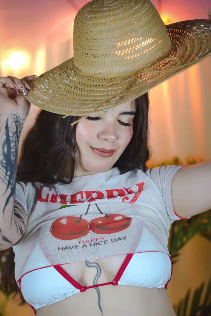 DaphneGlass — Smiling woman in a white graphic crop top and straw hat posing in warm, sunny lighting.