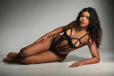 Curvy woman in black lace bodysuit reclining on a white studio floor with a moody, elegant aesthetic.