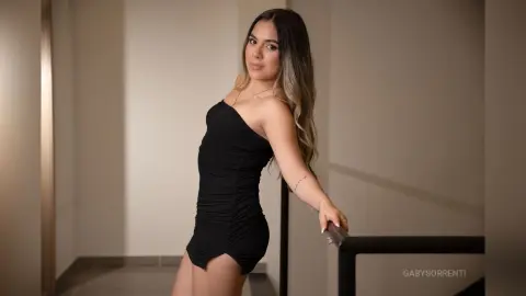 Young woman in a sleek black mini dress posing confidently in a modern minimalist hallway.