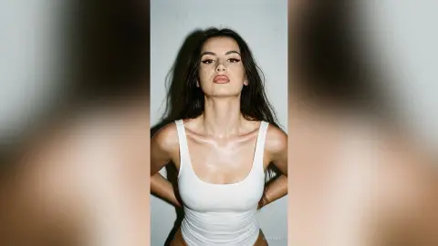 ZenyaSin poses in a white tank bodysuit with her long dark hair down against a plain light background.