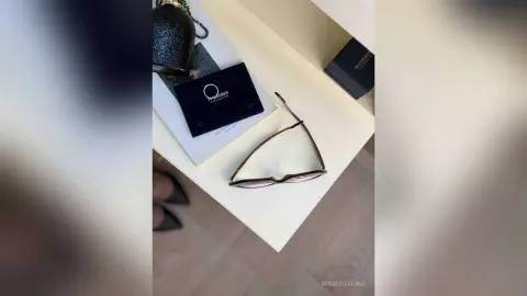 Elegant designer eyeglasses and luxury perfume bottle on a minimalist white vanity shelf.