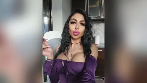 AvaNoah — AvaNoah poses in a purple low-cut top with long wavy dark hair while looking at the camera.