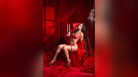 RoxannaRivera poses in red lingerie and red heels against a red curtain backdrop, showing off her long dark hair and toned legs.
