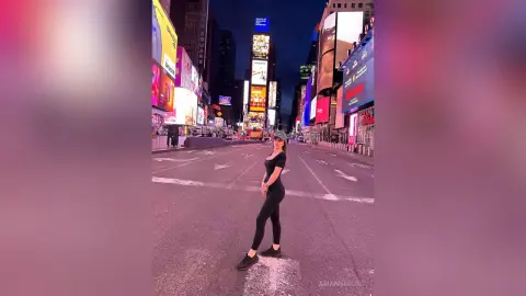 Stylish woman in black outfit standing on a neon-lit New York City street at night.
