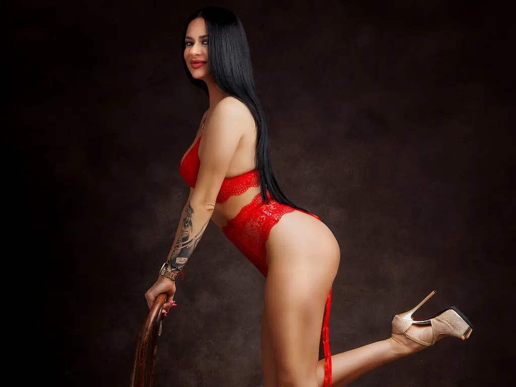 Glamorous woman in red lace lingerie and gold heels posing against a dark studio background.