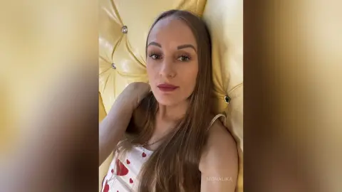 Young woman with long brown hair wearing a white tank top relaxing on a yellow tufted sofa.