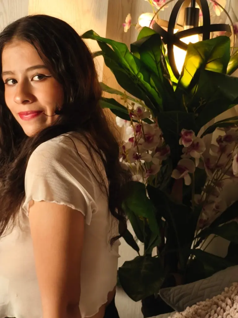 Dolly_bobssy poses with long dark hair, wearing a white top against a neutral background.