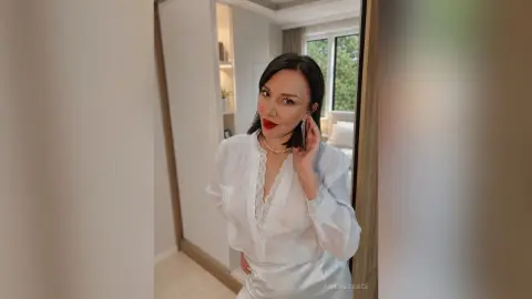 SimoniGrace poses in a white silk pajama set with lace trim, smiling in a bright room.