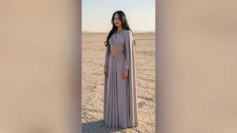 Elegant woman in a mauve wrap crop top and maxi skirt standing in a vast desert landscape at sunset.