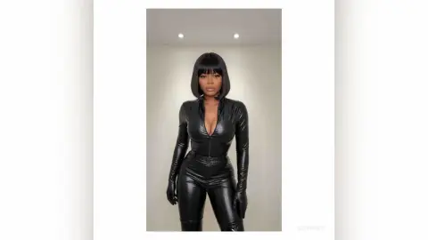 Stylish woman in a sleek black faux leather jumpsuit posing in a minimalist studio setting.