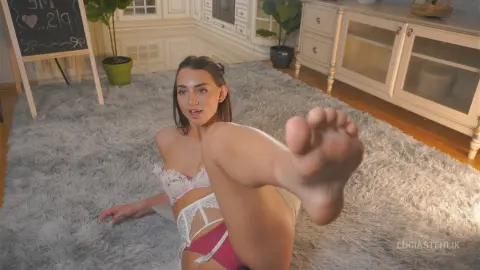 Young woman in white lace lingerie relaxing on a grey shag rug in a bright, cozy living room.