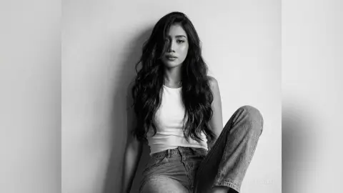 Moody black and white portrait of a woman with long wavy hair wearing a white tank top and denim jeans.