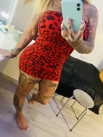 Woman with tattoos in a red leopard print mini dress taking a mirror selfie in a bright room.