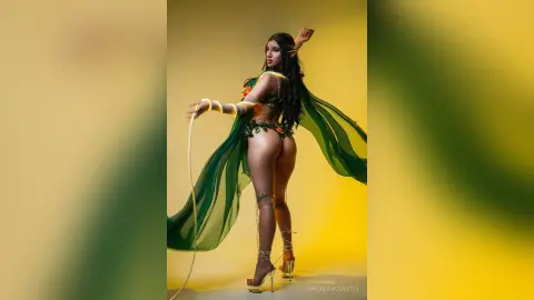 Elegant woman in a green floral bikini and flowing sheer cape posing against a vibrant yellow studio background.