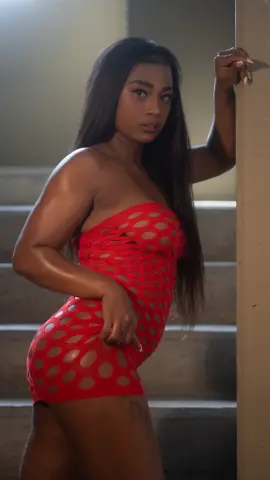 Young woman in a red polka dot mini dress posing in a moody indoor stairwell setting.