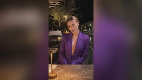 Elegant woman in a purple blazer sitting at an outdoor restaurant terrace at night.
