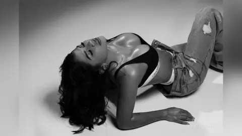 Glamorous woman in black Calvin Klein lingerie relaxing on a white floor in a moody black and white portrait.