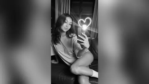 LeahReel — Young woman in casual t-shirt taking a moody black and white mirror selfie with a glowing heart light.