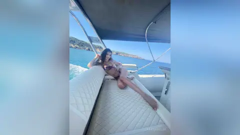 Relaxed woman in a bikini lounging on a white boat seat under a sunny blue sky on the ocean.