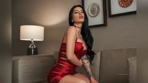 Glamorous woman in a red cutout dress posing on a sofa in a moody, dimly lit living room.