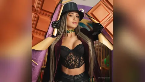 Glamorous woman in a black lace corset and top hat posing with giant chocolate bars in a playful mood.