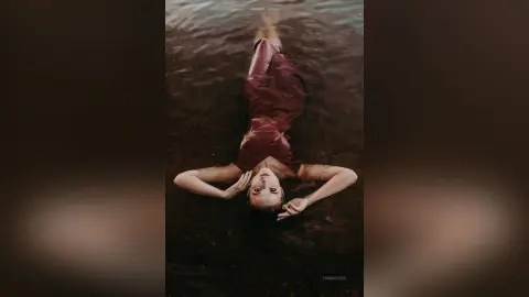 Dreamy portrait of a woman in a burgundy dress floating peacefully on dark water.