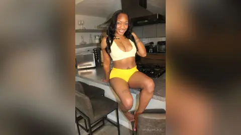 Smiling Black woman in a yellow bikini set posing in a modern kitchen setting.