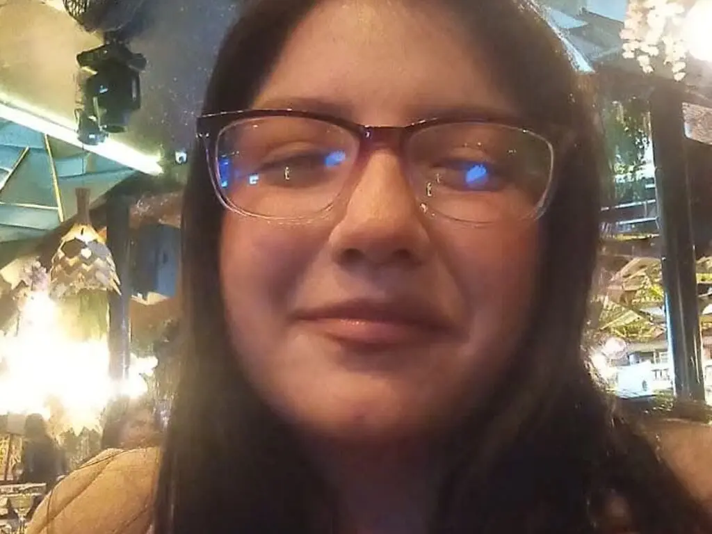 Smiling young woman with glasses in a cozy, dimly lit cafe setting.