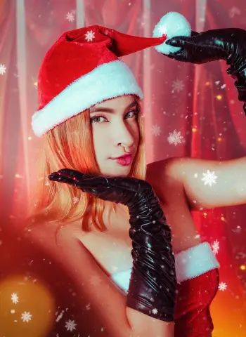 Glamorous woman in a red Santa hat and black gloves posing against a festive red holiday background.