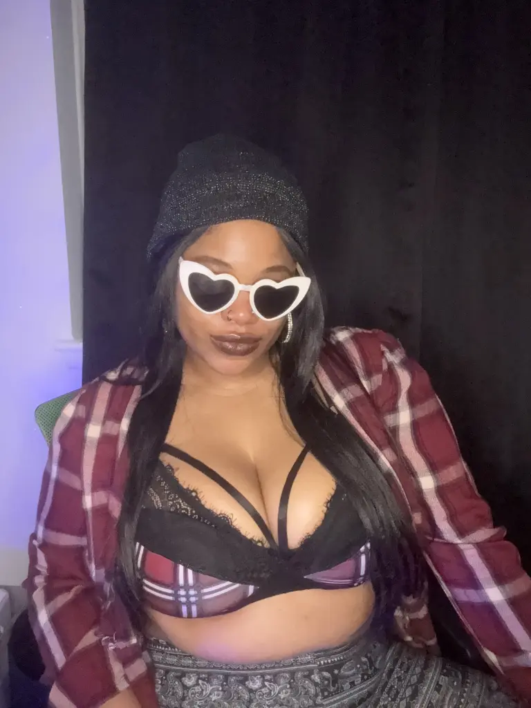 EmpressPhoenix wears heart-shaped sunglasses and a red plaid shirt, showing cleavage in a black lace bra while looking at the camera.