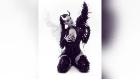 Woman in dark angel cosplay with large feathered wings and horns posing against a white background.