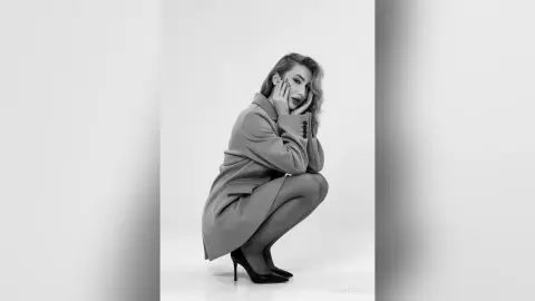 Elegant woman in a stylish wool coat and high heels posing against a white studio background in black and white.
