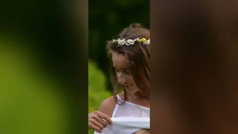 Young woman in a white tank top wearing a daisy flower crown in a lush green meadow with a dreamy mood.