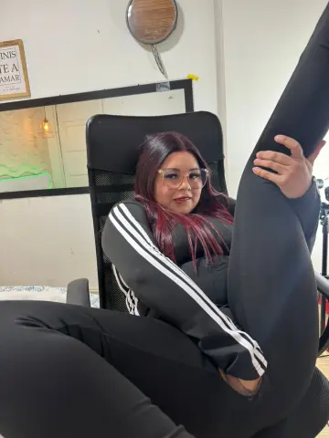 Smiling woman with red hair in black Adidas tracksuits relaxing in an office chair.