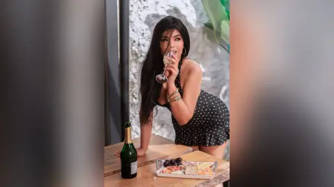 Elegant woman in a black polka dot dress sipping champagne at a luxury outdoor brunch setting.