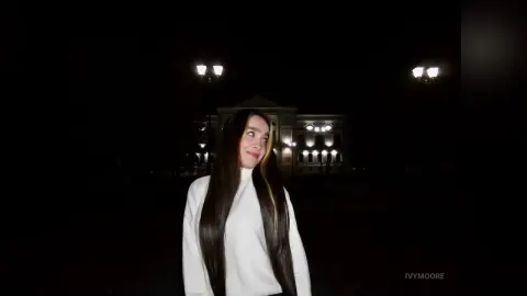 Young woman in a white turtleneck smiling at night in front of a lit classical building.