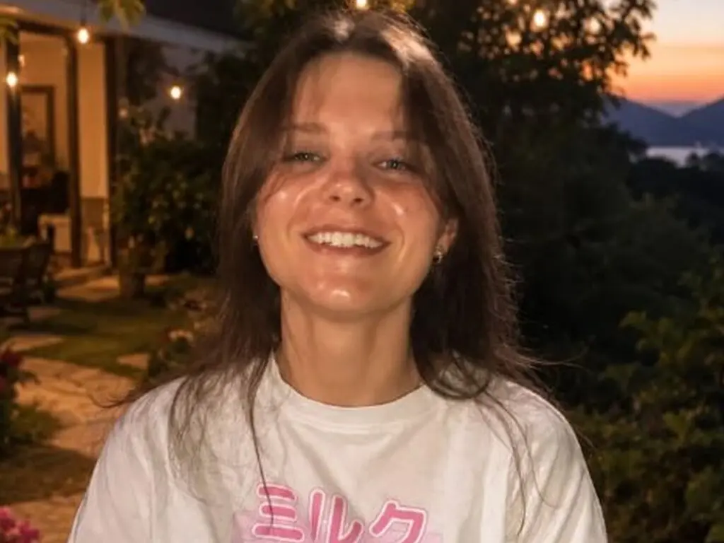 Smiling young woman in a white graphic t-shirt enjoying a warm evening outdoors in a garden setting.