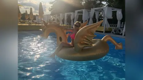 MilenaBia poses in a pink bikini while sitting on a large gold dragon-shaped pool float in a swimming pool.