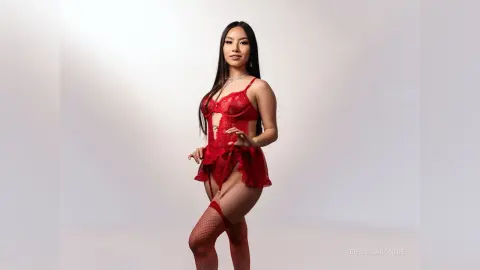 Beautiful woman in a red lace bodysuit and fishnet stockings posing against a white studio background.