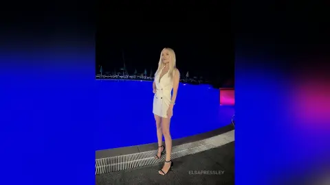 Blonde woman in a chic white mini dress standing on a dark stage with blue cinematic lighting.