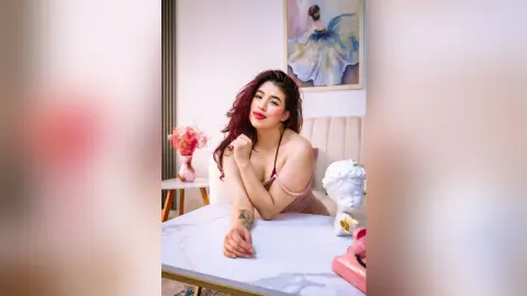 Smiling woman in a pink dress sitting at a marble table in a bright, aesthetic room.