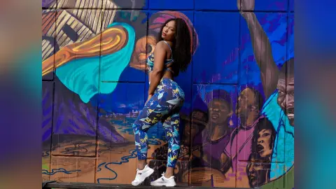 Stylish woman in blue patterned leggings and sports bra posing against a colorful urban street art mural.