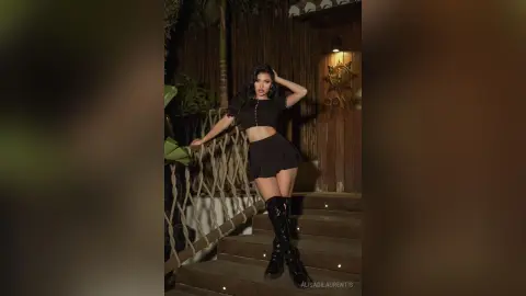 Stylish woman in a black crop top and mini skirt posing on wooden stairs in a tropical evening setting.